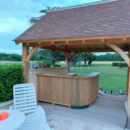 Bar en bois sous un auvent, entouré de verdure et avec un espace de détente.